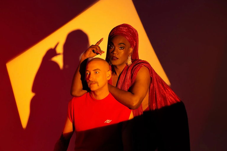 Australian electronic duo Electric Fields posing together in dramatic red and yellow lighting for a promotional studio portrait shoot.